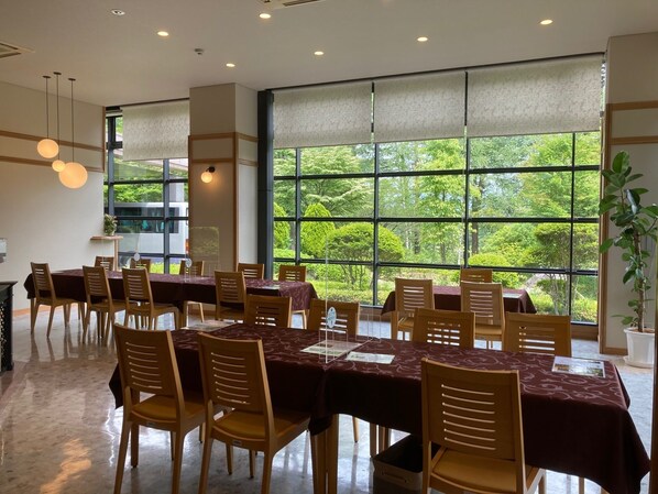 Un comedor con ventanas amplias, sillas de madera y mesas cubiertas con manteles oscuros.