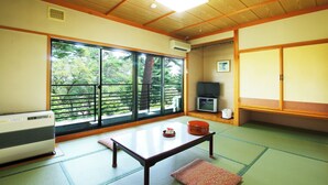 Una habitación tradicional japonesa con suelo de tatami, puertas correderas, una mesa y un recipiente rojo, y un televisor.
