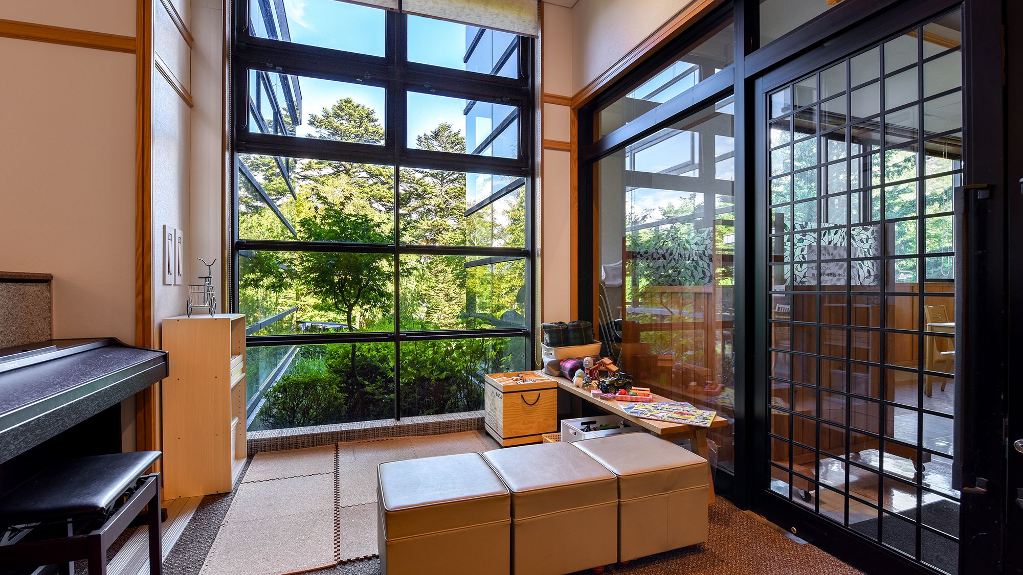 A room with large windows, a piano, a wooden cabinet, and a small table with various items.