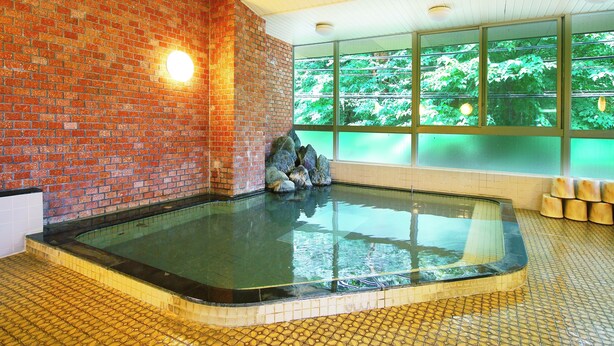 Un área de spa con pared de ladrillo, un jacuzzi con paredes de vidrio y vistas a la vegetación a través de amplias ventanas.
