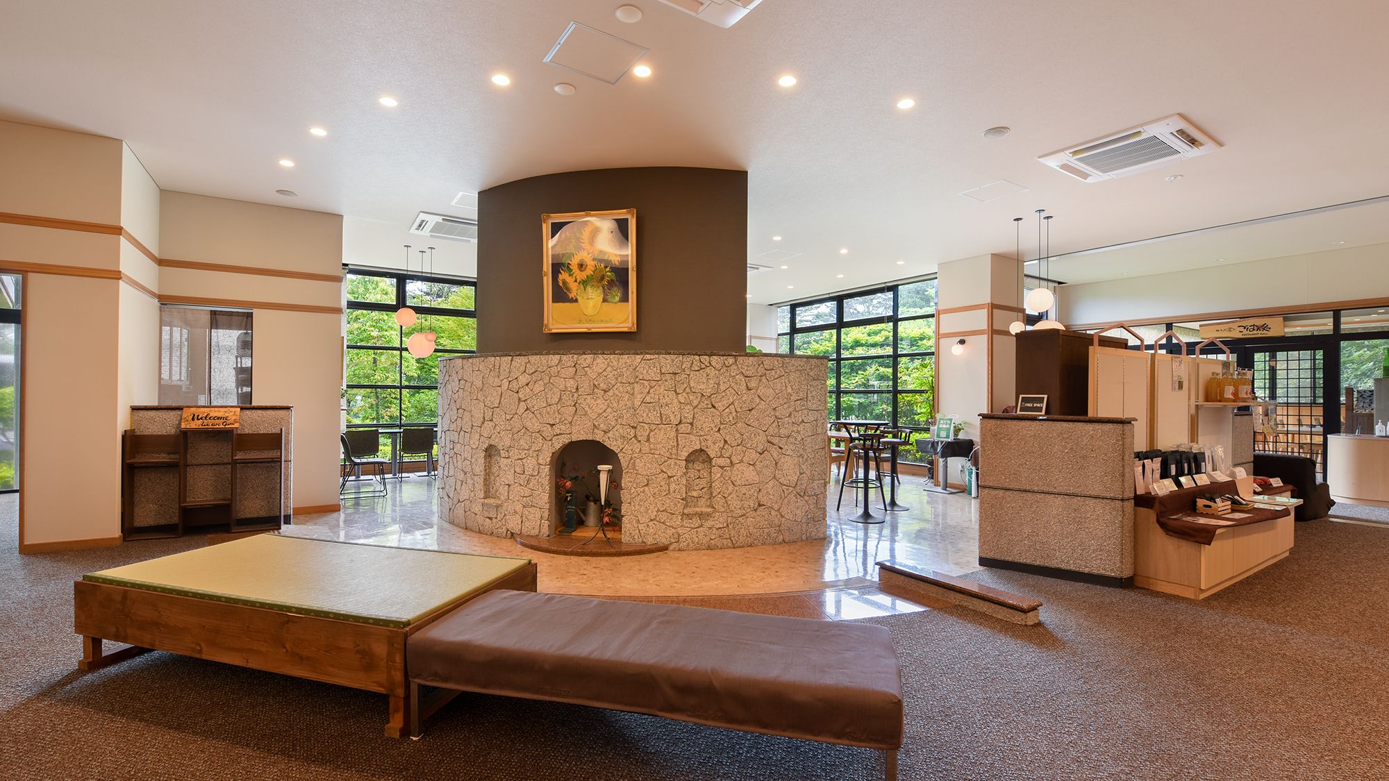 A modern interior with a stone fireplace, seating area, and large windows offering a view of greenery.