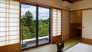 Una habitación japonesa tradicional con suelo de tatami, una puerta corredera con vistas a la vegetación y un aire acondicionado instalado en el techo.