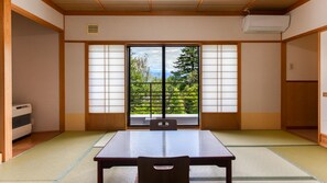 Una habitación tradicional japonesa con suelo de tatami, puertas correderas shoji y vistas a la vegetación exterior.