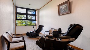 A room with two massage chairs, a wooden chair, a window with a view of trees, and a framed picture on the wall. - Hayataro Onsen Komagane Retreat Suzuranso (Komagane)