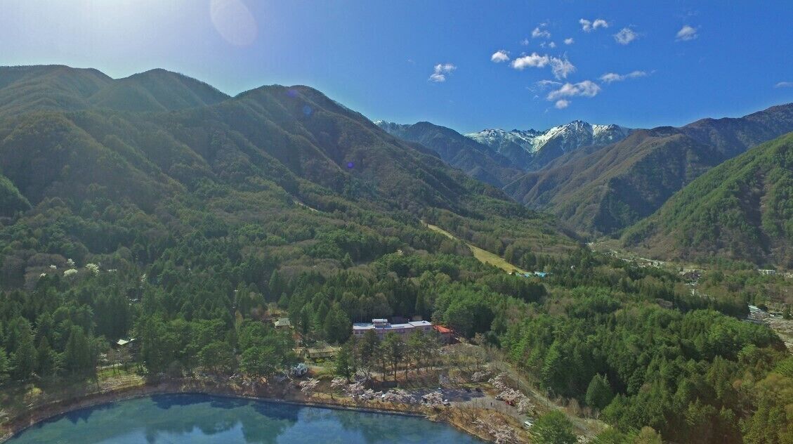 A mountainous landscape with a lake, a small building, and distant snow-capped peaks.