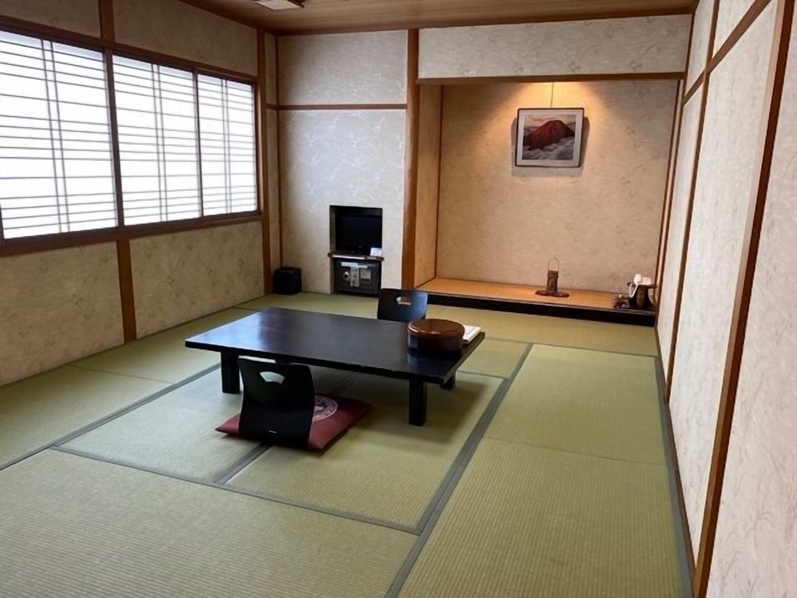A tatami mat room with a low table, a television, and a framed picture on the wall.