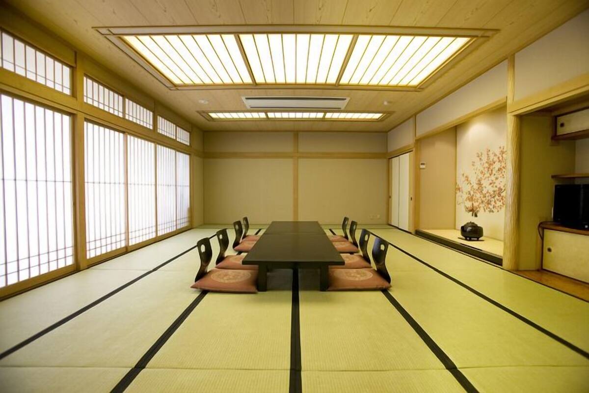 Ein traditioneller japanischer Raum mit Tatami-Bodenbelag, einem langen Tisch und Schiebetüren.