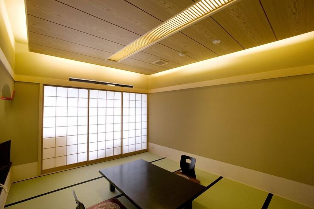 Ein traditioneller japanischer Raum mit Tatami-Bodenbelag, einem niedrigen Tisch, einer Schiebetür und einer Decke mit eingelassener Beleuchtung.
