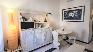 Una habitación con un armario blanco, un televisor de pantalla plana, una lámpara, un cuadro abstracto enmarcado y una mesa redonda con sillas.