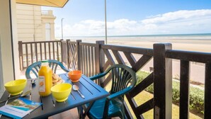 Una mesa con cuencos, una botella y una cuchara en un balcón con vista a la playa.