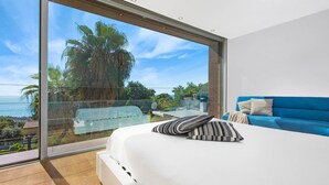 A bedroom with a large sliding glass door leading to a balcony overlooking the sea.