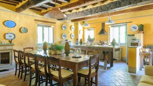 A rustic kitchen with wooden beams, a dining table with chairs, and various kitchen items. - Villa Montanina - Relax in Tuscany (Castel Focognano)