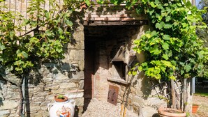 A stone building with a brick chimney, a large terracotta pot with a plant, and a wooden trellis with climbing plants. - Villa Montanina - Relax in Tuscany (Castel Focognano)