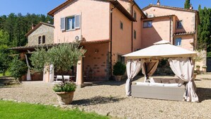 A two-story house with a stone extension, outdoor seating, and a covered area with a sofa. - Villa Montanina - Relax in Tuscany (Castel Focognano)