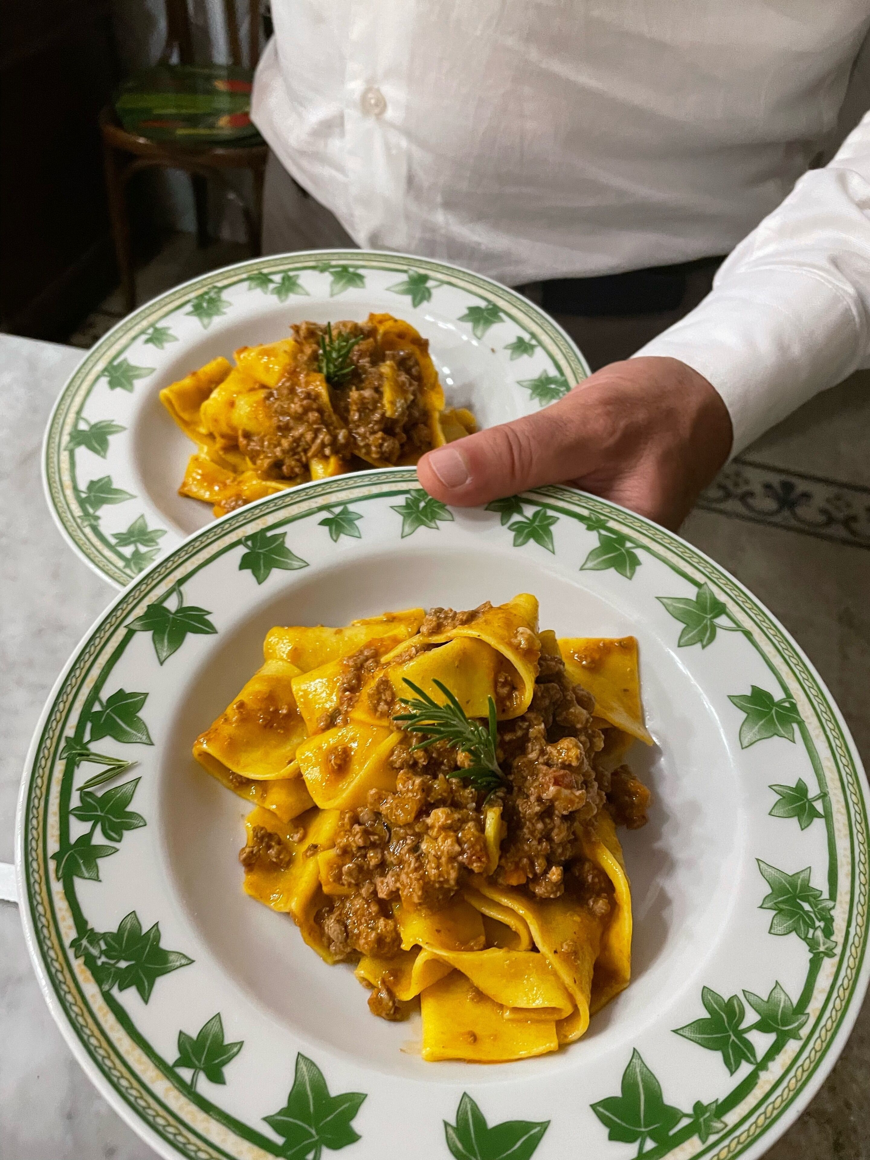 Two plates of pasta with a meat sauce, held by a person.