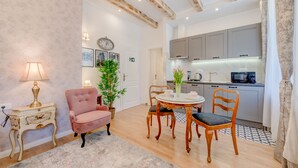 A cozy living room with a pink armchair, a round dining table, and a small kitchen area with grey cabinets and a microwave. - Le Monde Luxury Accommodation (Split)