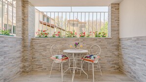 A small balcony with a white table and chairs, a window with a view of buildings, and a tiled floor. - Le Monde Luxury Accommodation (Split)