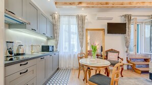 A modern kitchen with a dining area, featuring a round table with chairs, a television mounted on the wall, and a staircase leading to an upper level. - Le Monde Luxury Accommodation (Split)