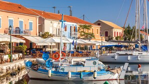 A harbor with boats docked, a building with a red roof, and a white building with blue shutters. - Villa Anthia (Kefalonia)