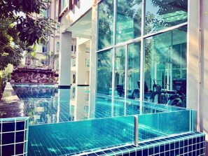 Un hôtel moderne doté d’une piscine à débordement à ciel ouvert, d’un mur en pierre et d’équipements de musculation visibles à travers la vitre.