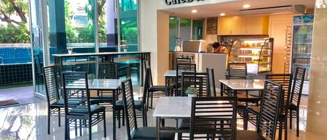 Un CafeDeluxe con una decoración moderna, que presenta paredes de vidrio, sillas negras y un suelo de baldosas limpias.