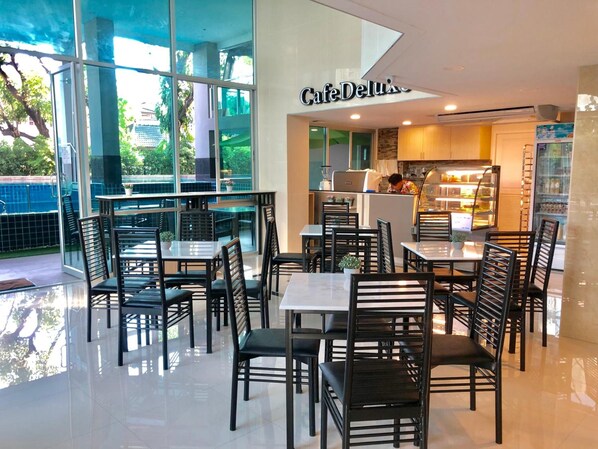 Un CaféDeluxe au décor moderne, avec des murs en verre, des chaises noires et un sol carrelé, sobre et élégant.