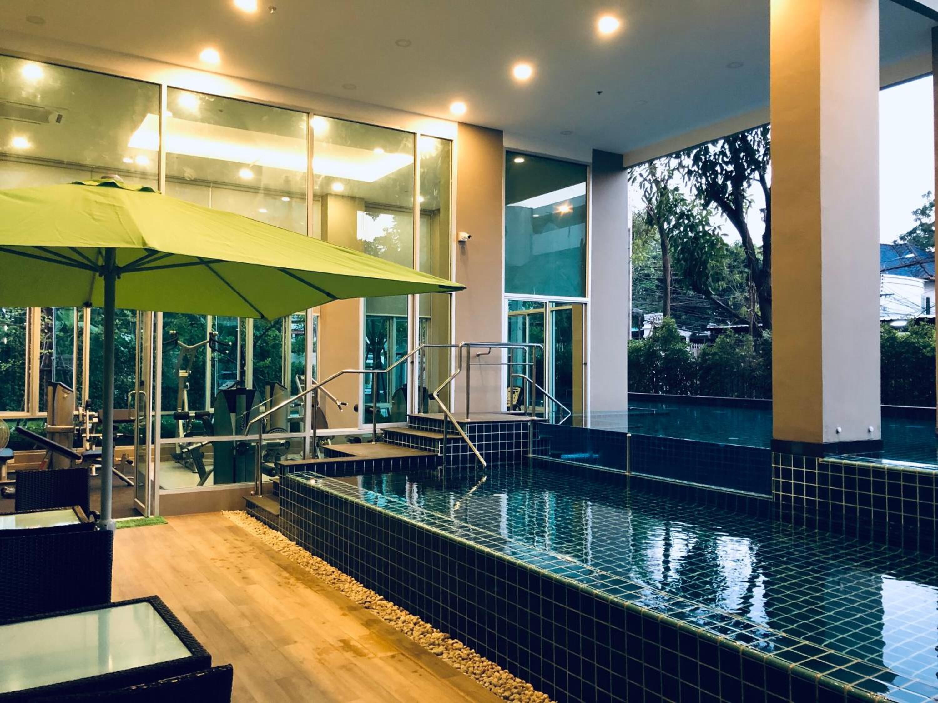 An indoor swimming pool with tiled walls, a wooden floor, and a glass enclosure with exercise equipment.