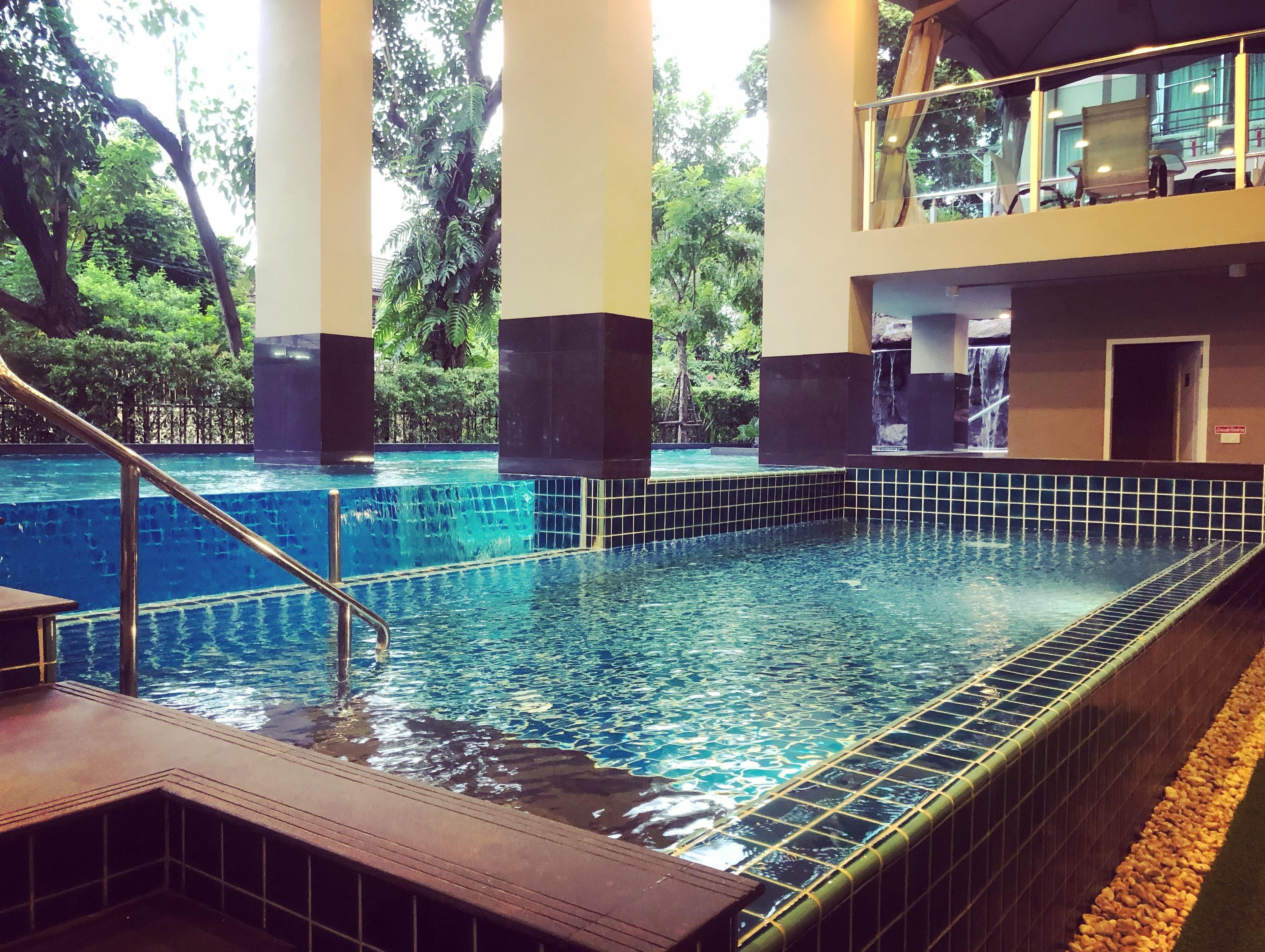 A swimming pool with a tiled edge, surrounded by pillars and a glass railing.