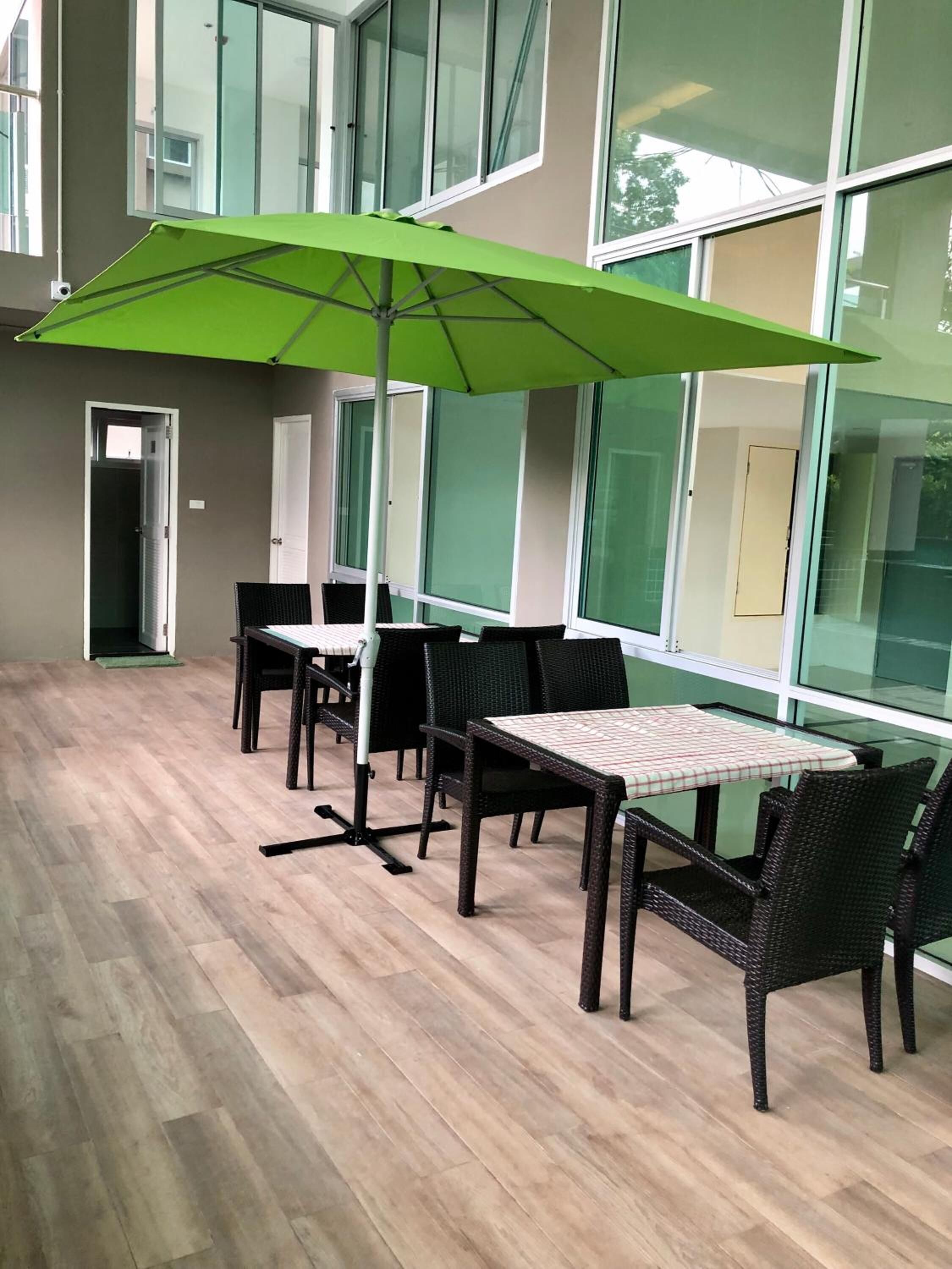 Un área de estar interior moderna con mesas, sillas, ventanas grandes y un paraguas verde.