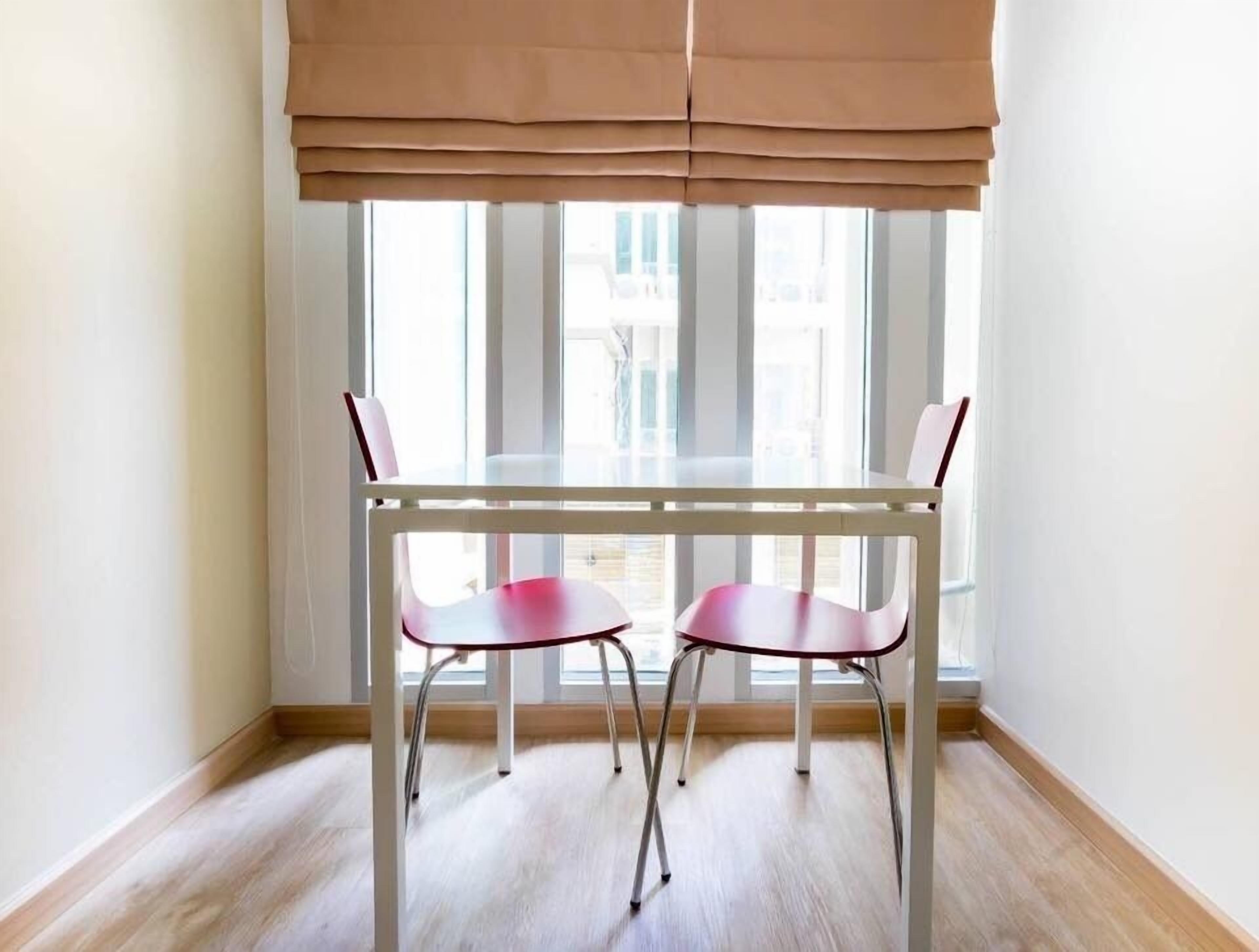 Ein Essbereich mit Tisch und zwei Stühlen, einem Fenster mit Jalousien und Holzdielen.