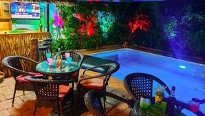An outdoor bar area with wicker furniture, a pool, and a colorful wall with plants. - Siri Villas (Pattaya)