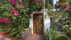 A traditional wooden door with intricate carvings, surrounded by lush greenery and vibrant pink bougainvillea flowers. - Siri Villas (Pattaya)