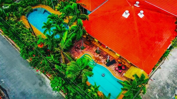 An aerial view of a resort with two swimming pools surrounded by lush greenery and palm trees. - Siri Villas (Pattaya)