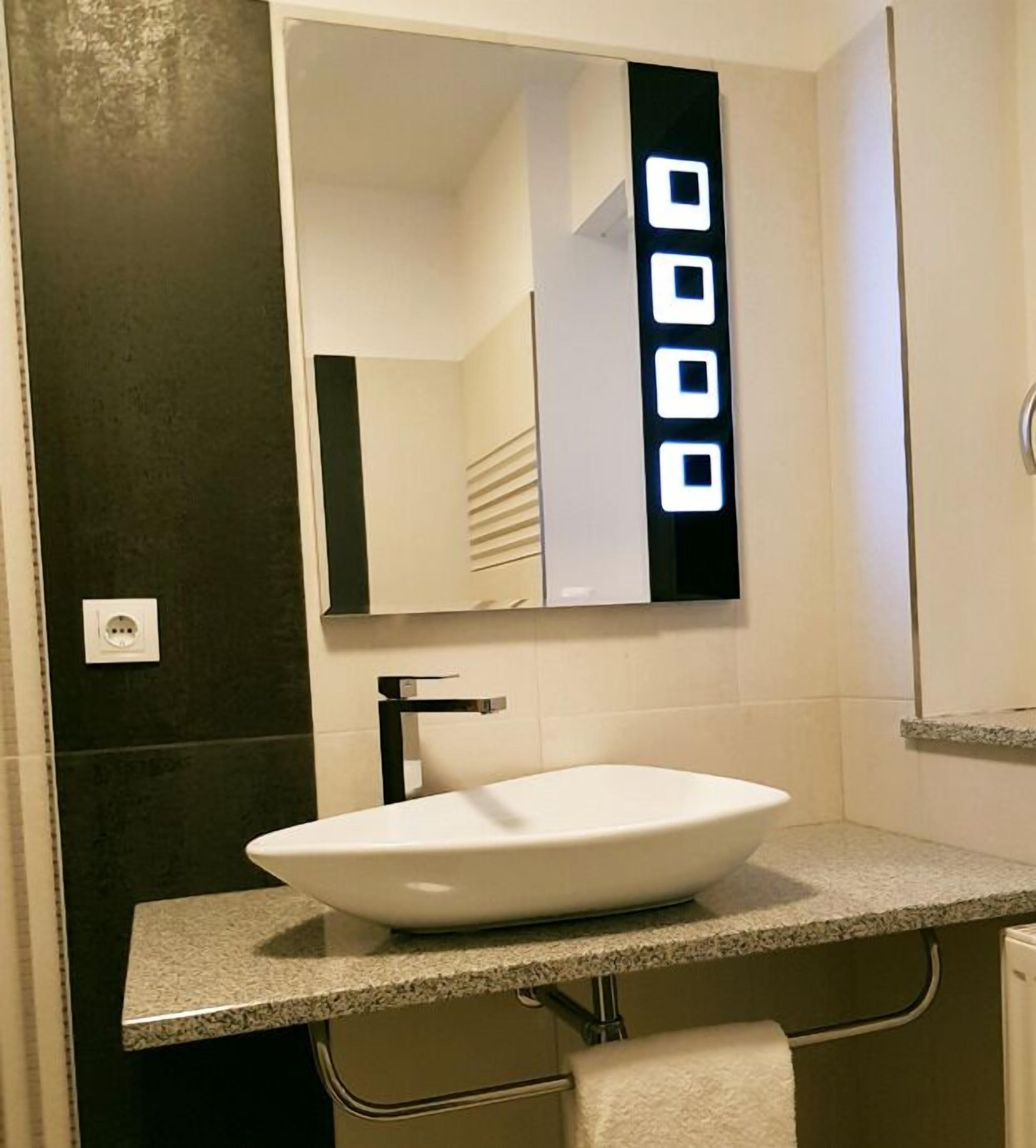 A modern bathroom with a white sink, dark walls, and a mirror with illuminated square lights.
