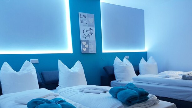 A hotel room with two beds, white bedding, and a blue accent wall. - Blissberg Winterberg (Winterberg)