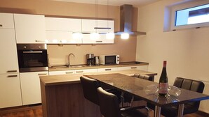 A modern kitchen with white cabinets, a built-in oven, a microwave, and a dining area with a table and chairs. - Blissberg Winterberg (Winterberg)