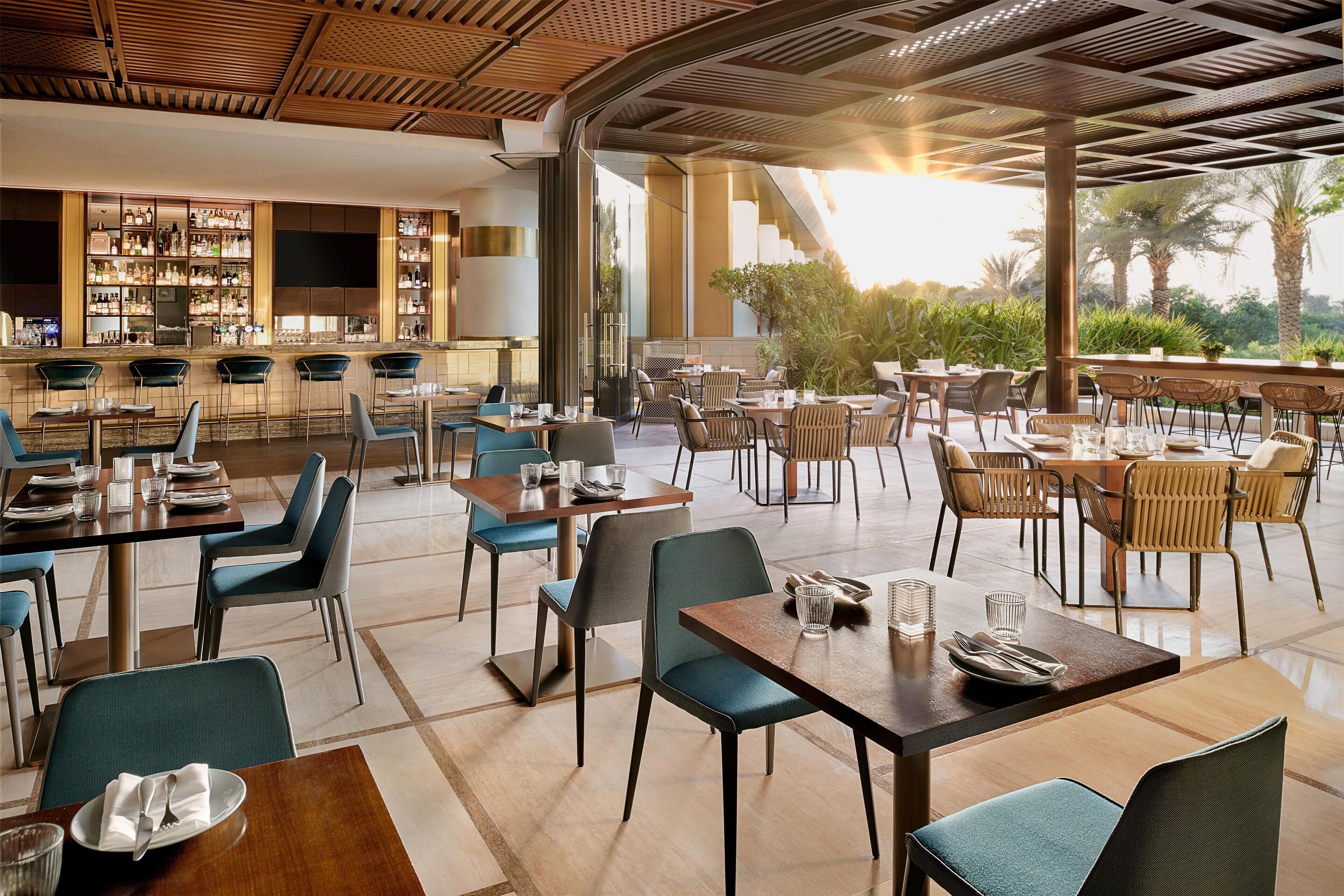 Un restaurant doté de plusieurs espaces de restauration, d’un bar et offrant une vue sur des palmiers.