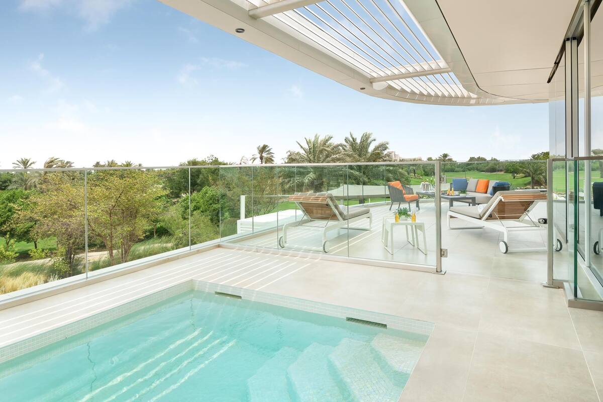 A modern outdoor pool area with glass railings, a lounge chair, and a dining table.