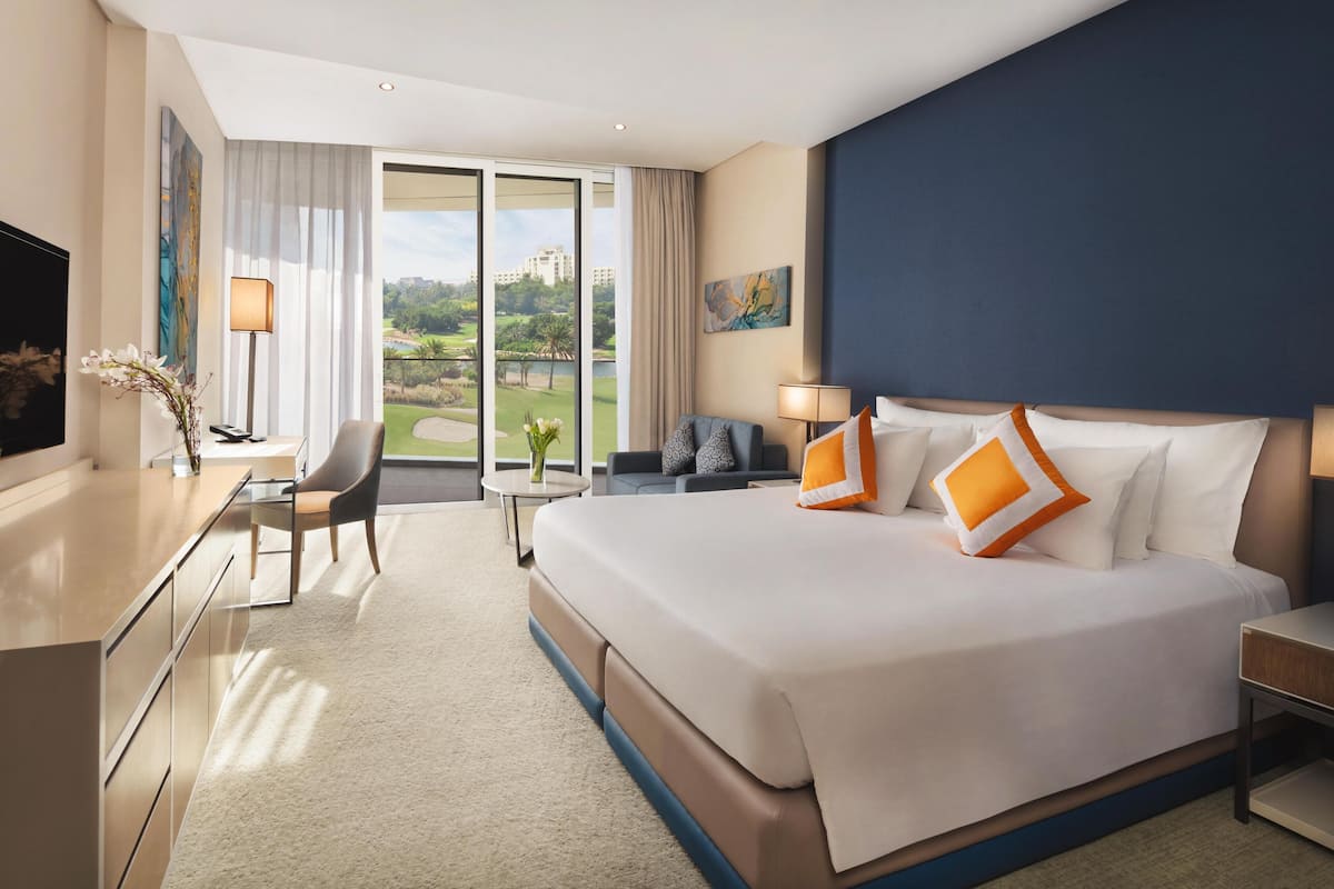 A hotel room with a large bed, a desk, a chair, a small table, and a view of a golf course through the window.