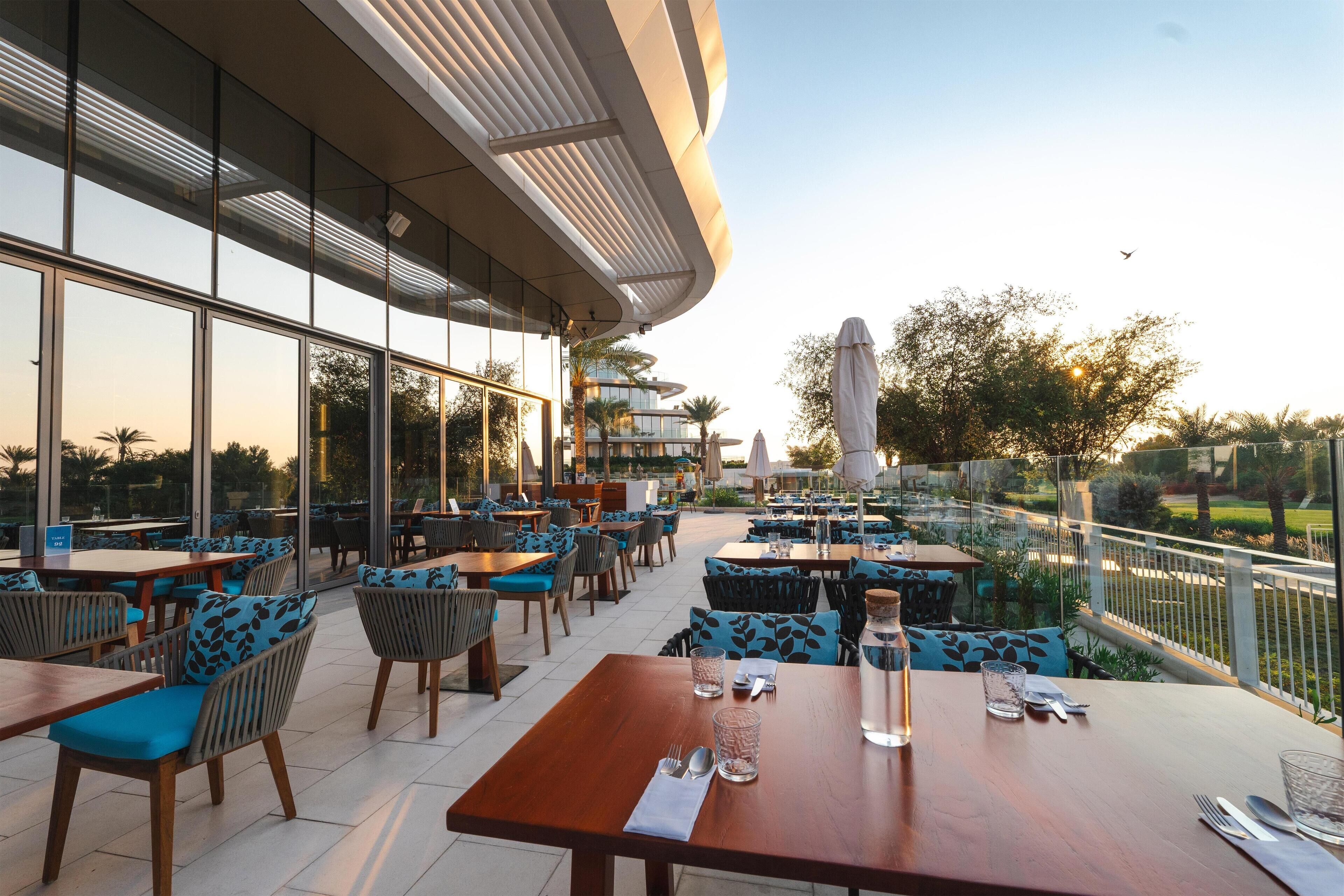 Un espace extérieur aménagé pour les repas, avec des tables et des chaises, de grandes fenêtres et une vue sur le paysage environnant.