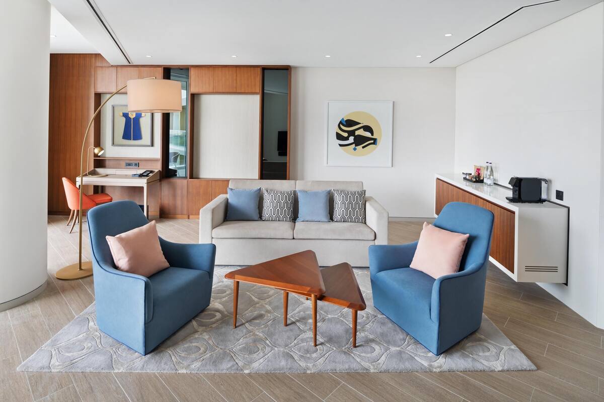 A modern living room with two blue armchairs, a grey sofa, and a wooden coffee table.