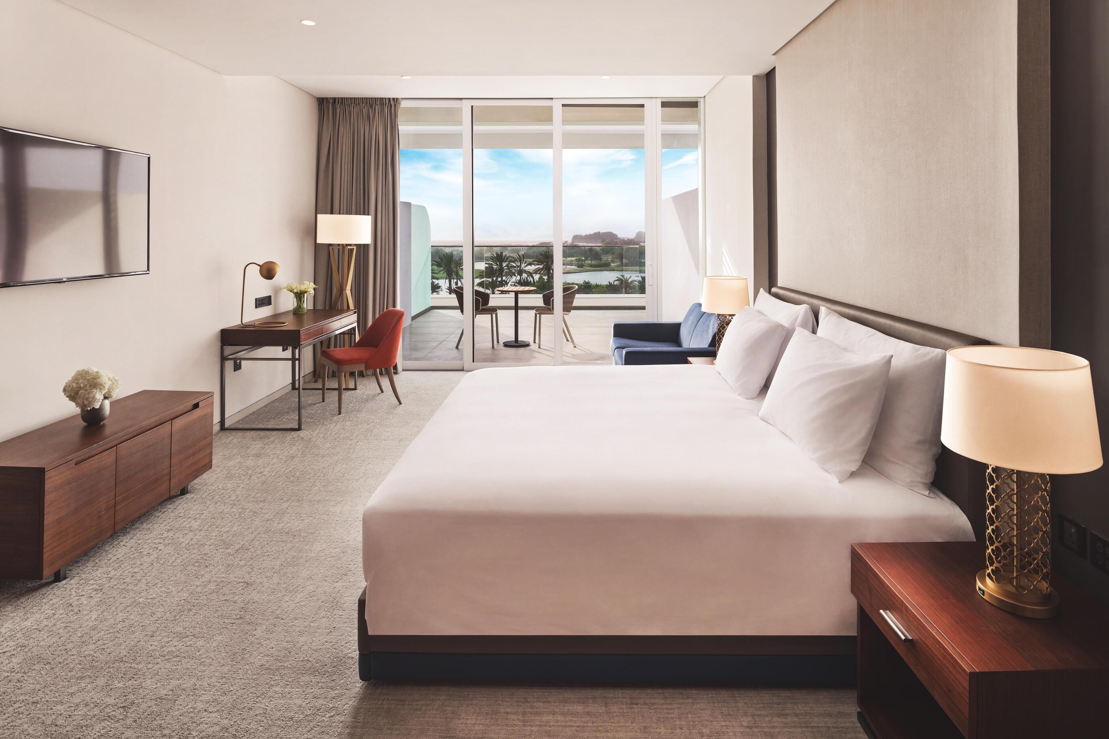 Hotelkamer met een groot bed, een bureau met stoel, een televisie en uitzicht op de omgeving.