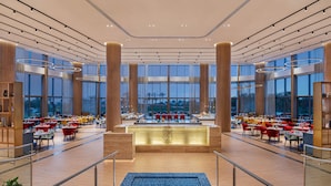 Eine geräumige Hotelhalle mit einer zentralen Rezeption, großen Fenstern und einem blau teppichbelegten Bereich.