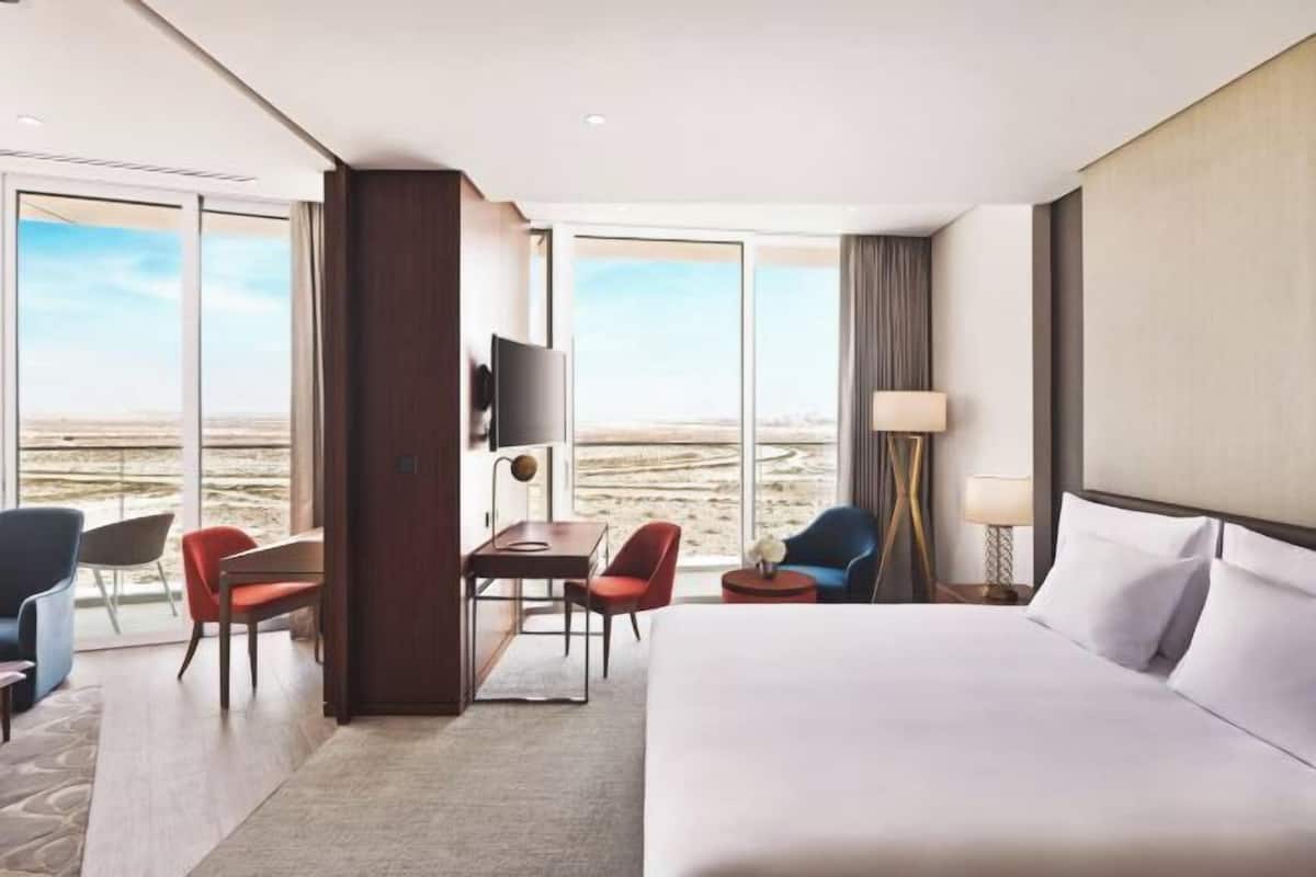 A hotel room with a large bed, a desk with chairs, a TV, and a view of the desert.