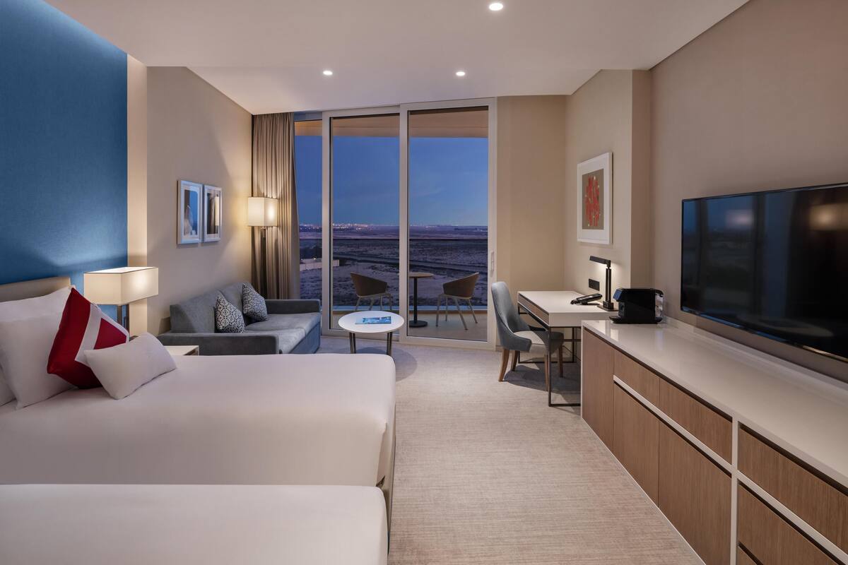 A hotel room with a bed, a desk, a chair, a TV, and a view of the cityscape.