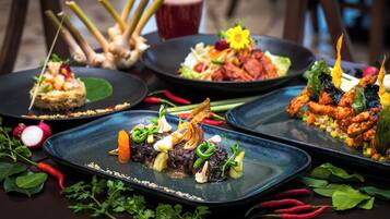 Une table dressée avec divers plats, notamment une salade, un plat de viande et un dessert, le tout agrémenté d’herbes et de légumes.
