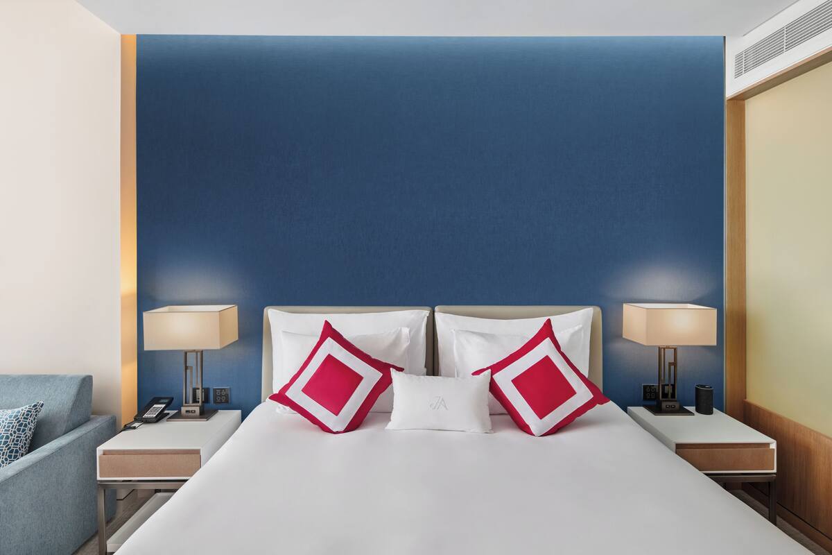 A hotel room with a large bed, two nightstands, a lamp, and a blue accent wall.