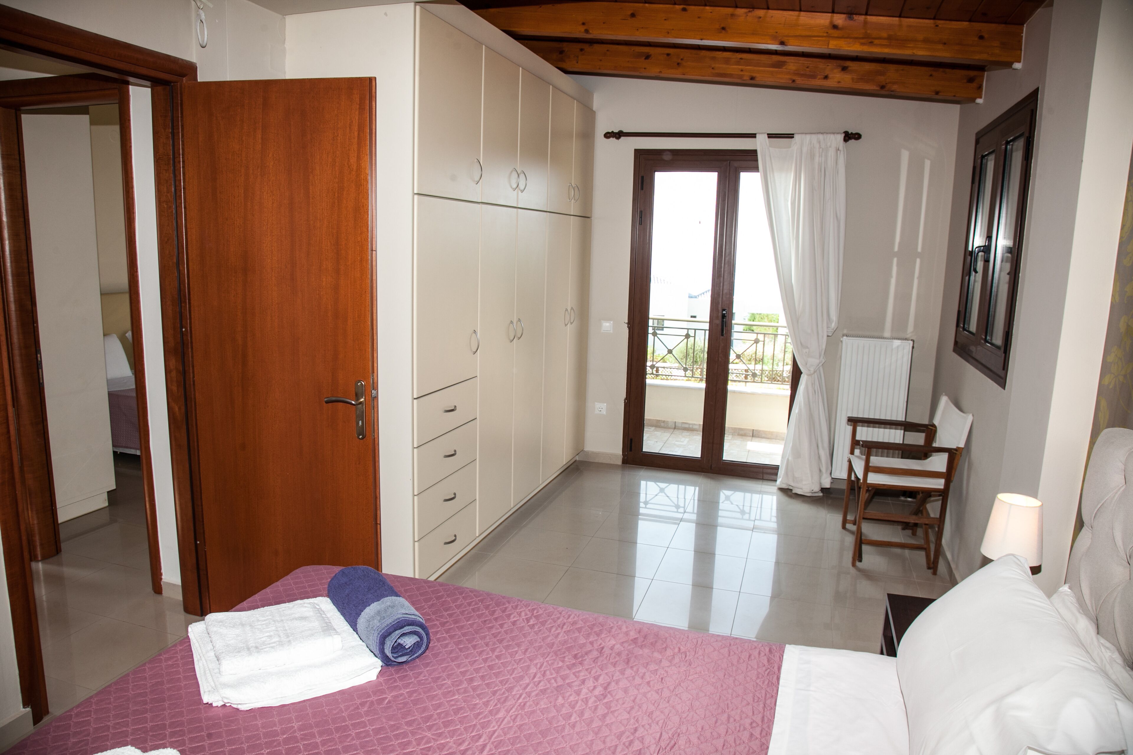 A bedroom with a bed, a wardrobe, a chair, and a balcony with a view.