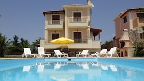 A pool area with lounge chairs and a yellow umbrella. - Villa Artemis (Kefalonia)
