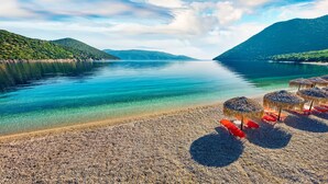 A beach with clear water, pebbles, and thatched umbrellas. - Villa Artemis (Kefalonia)